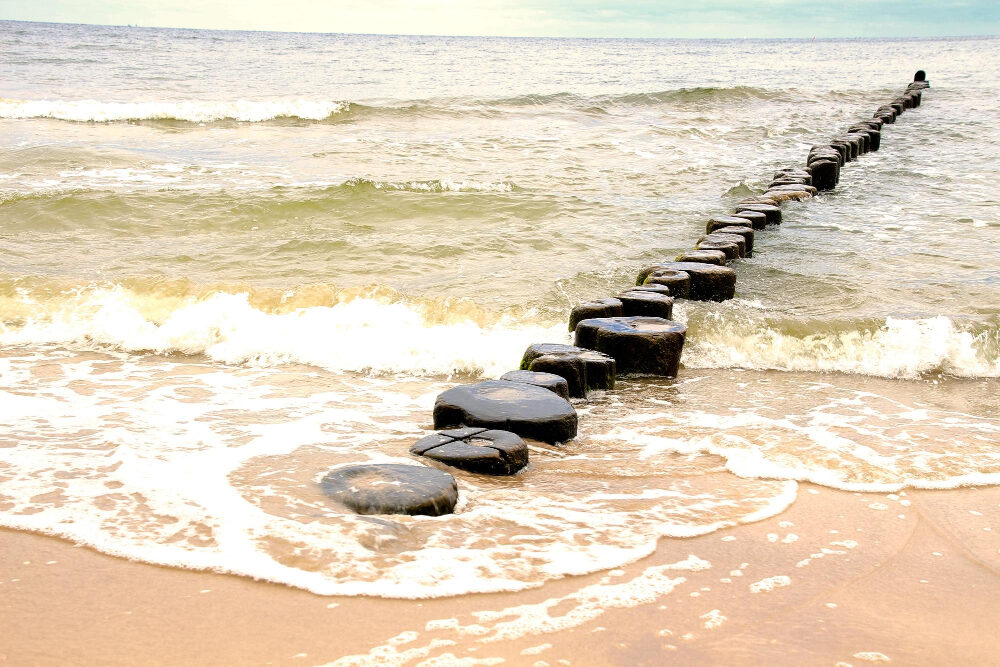 Rij houten golfbrekerpalen die vanaf het strand de zee in loopt